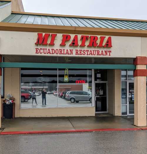 Exterior of Mi Patria, an Ecuadorian restaurant, featuring a large sign and an open door. Rainy weather visible.