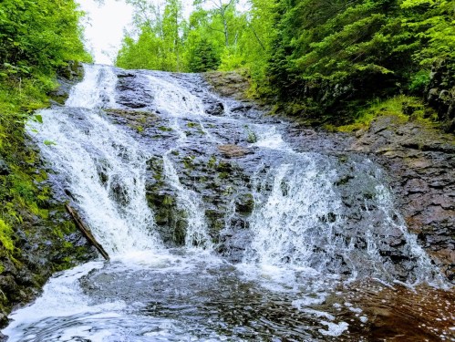 A serene waterfall cascading over rocky terrain, surrounded by lush green trees and foliage.
