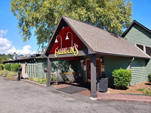 Exterior of a restaurant named "Gilhoun's," featuring a red sign and a green building surrounded by trees and landscaping.