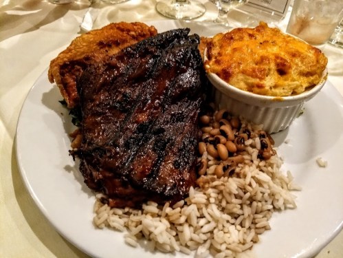 A plate featuring grilled meat, fried chicken, rice, black-eyed peas, and a baked dish.
