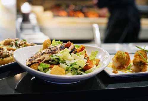 A vibrant salad with grilled chicken, lettuce, tomatoes, and croutons, served in a restaurant setting.