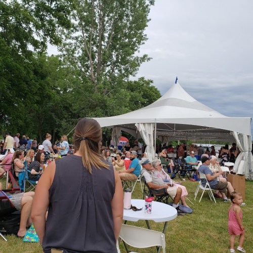 A crowd gathers under a large tent at an outdoor event, with people seated and enjoying the atmosphere.