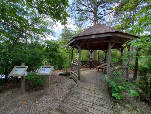 A wooden gazebo surrounded by trees, with informational signs nearby and a peaceful natural setting.