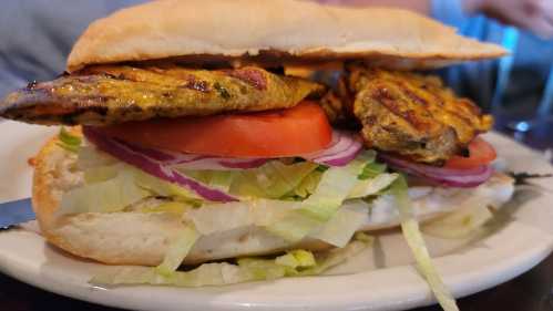 A sandwich with grilled chicken, lettuce, tomato, and onion, served in a soft bun on a plate.