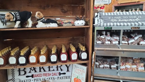 A rustic display featuring baked goods, syrups, and decorative items, with stuffed animals and a sign about homemade gifts.