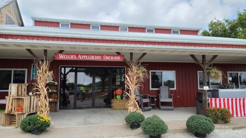 Welch's Appleberry Orchard storefront with red siding, pumpkins, and fall decorations under a cloudy sky.