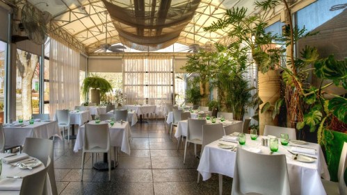 Bright, modern restaurant interior with white tables, green accents, and lush plants, creating a fresh, inviting atmosphere.