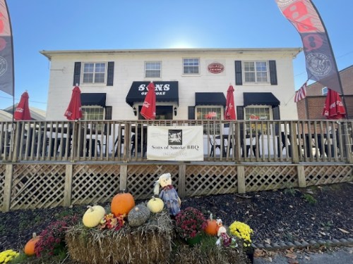A BBQ restaurant with outdoor seating, decorated with pumpkins and flowers, under a clear blue sky.