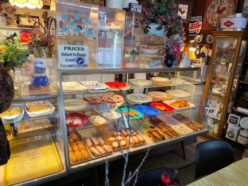 A display case filled with various baked goods and desserts, with colorful plates and a sign about prices.