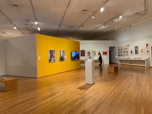 A spacious art gallery featuring colorful walls, framed artworks, and visitors exploring the exhibits.