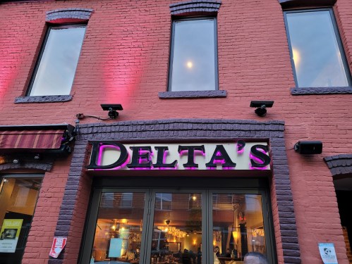 Exterior of Delta's restaurant, featuring a brick facade and large windows, with purple lighting above the entrance.