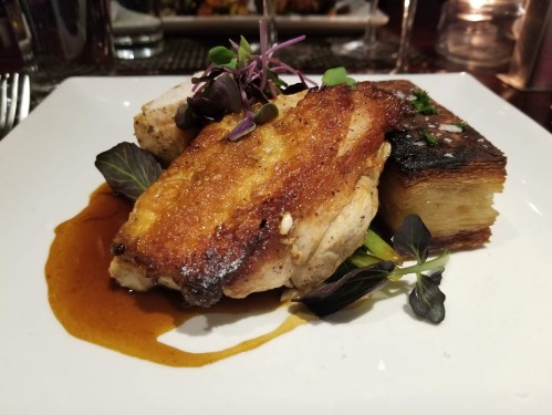 A plated dish featuring crispy chicken, garnished with microgreens and served with a side of roasted potatoes.