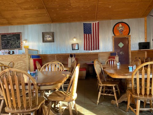 Interior of a rustic restaurant featuring wooden tables, an American flag, and cowboy-themed decor on the walls.