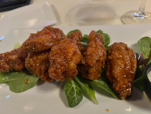 A plate of glazed chicken wings served on a bed of greens, accompanied by a small container of dipping sauce.