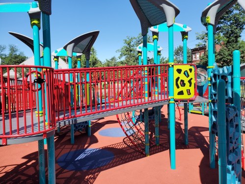 Colorful playground equipment with slides, climbing structures, and a bridge under a clear blue sky.