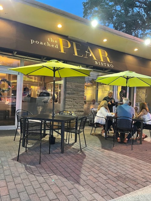 Outdoor dining scene at The Poached Pear Bistro, featuring tables with yellow umbrellas and patrons enjoying their meals.