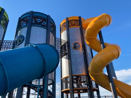 Colorful playground structure featuring a blue slide and an orange slide against a clear blue sky.