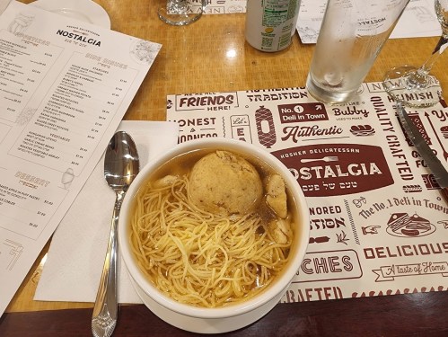 A bowl of noodle soup with a meatball, placed on a table with menus and a drink.