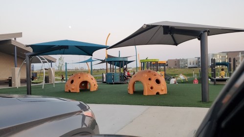 Playground with colorful equipment, including dome structures and shaded areas, set against a clear sky.