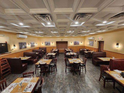 Interior of a restaurant featuring wooden tables, booths, and a coffered ceiling, with menus on each table.