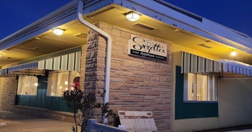 Exterior of Suzette's restaurant, featuring a stone facade, awnings, and illuminated windows at dusk.
