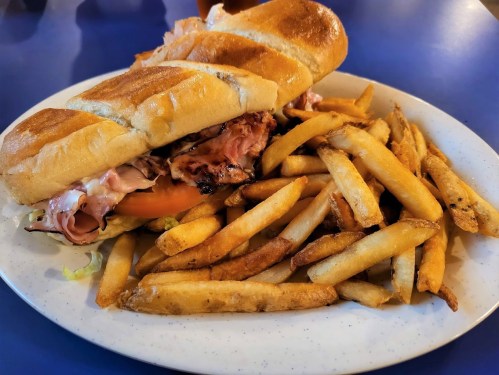 A toasted sandwich filled with meat and vegetables, served with a side of golden, crispy French fries.