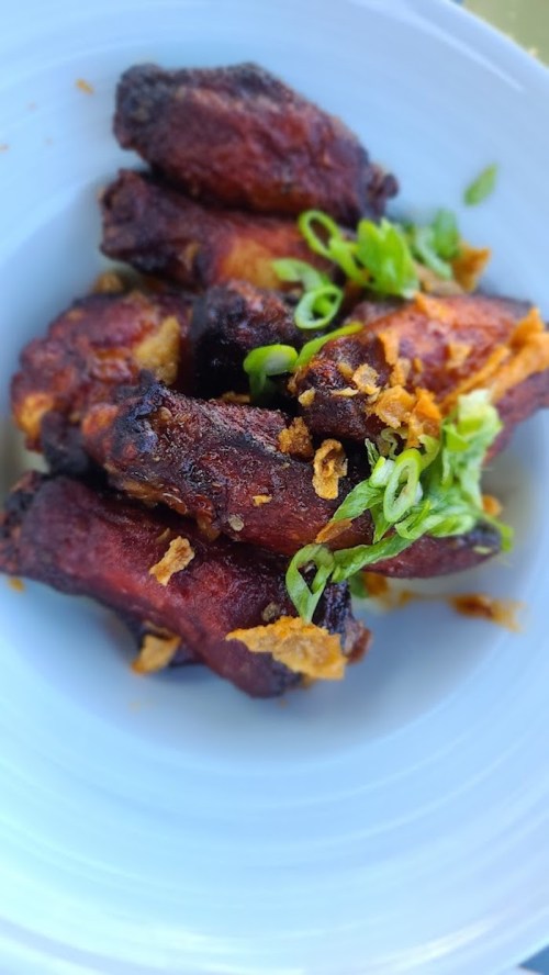 A plate of crispy chicken wings garnished with green onions and fried garlic.