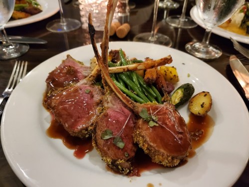 A plate of rack of lamb with a herb crust, served with green beans, roasted potatoes, and a rich sauce.