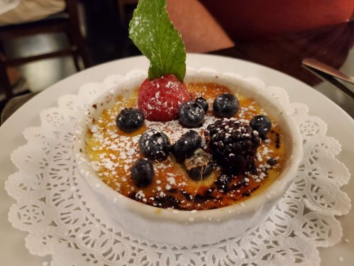 A creamy dessert topped with berries and mint, served in a white dish on a lace doily.