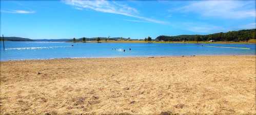 A serene lake scene with a sandy shore, clear blue water, and a few people enjoying the outdoors under a bright sky.