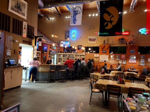 A cozy bar interior with patrons seated at tables and the bar, featuring various beer signs and flags on the walls.