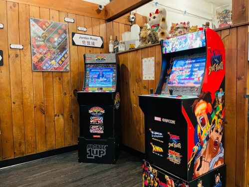 Two arcade machines in a wooden-paneled room, featuring classic games like X-Men and Street Fighter.