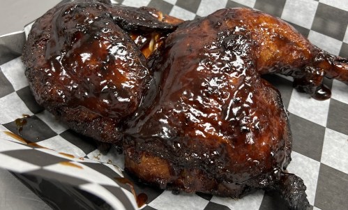 Two pieces of glazed, barbecued chicken on a black and white checkered paper.