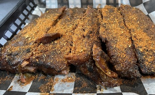 Close-up of seasoned, smoked ribs arranged in a black basket lined with checkered paper.