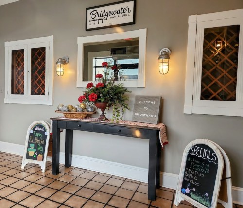 Welcoming entrance of Bridgewater Bar & Grill with floral decor, chalkboards, and a mirror on the wall.