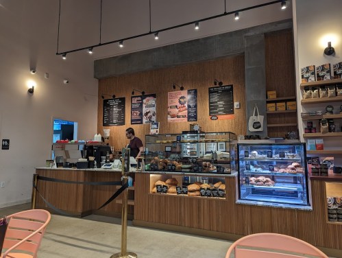 A cozy café interior with a counter displaying pastries, a barista at work, and menu boards on the wall.