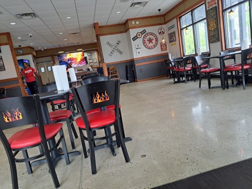 A mostly empty restaurant with black chairs featuring red seats, a TV in the background, and a staff member visible.