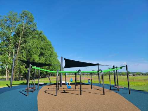 A colorful playground with green equipment and shade sails, set in a grassy area under a clear blue sky.