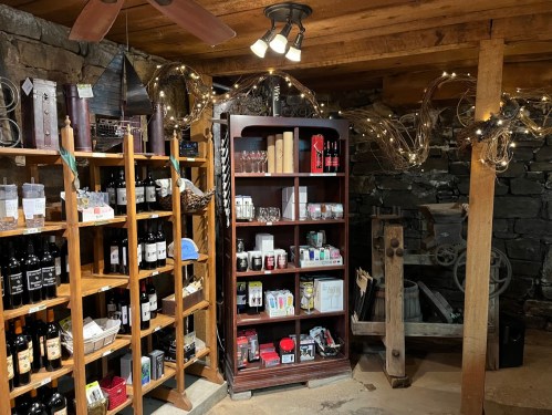 A cozy cellar with wooden shelves displaying wine bottles and various gift items, illuminated by soft lights.