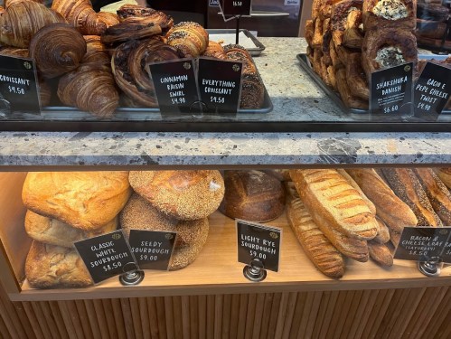 A bakery display featuring various pastries and loaves of sourdough bread with price tags.