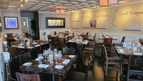 A cozy restaurant interior with wooden tables set for dining, soft lighting, and decorative wall art.