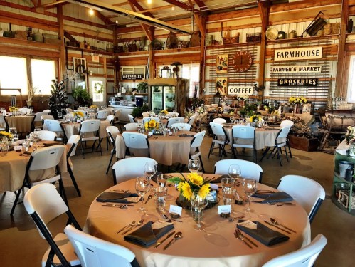 A rustic event space with round tables set for dining, decorated with sunflowers and vintage farmhouse decor.