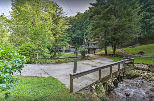 A serene landscape featuring a bridge over a stream, surrounded by lush greenery and rustic buildings in the background.