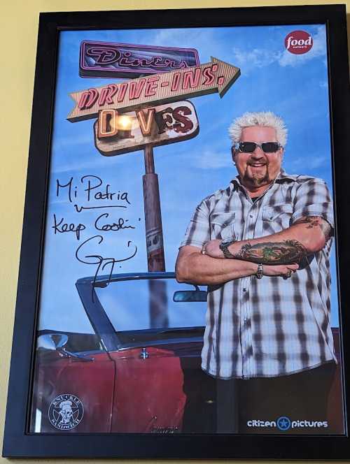 A framed photo of a man with spiky hair and sunglasses, standing next to a classic car, signed with a personal message.