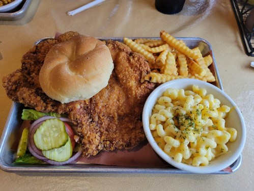 A tray with a crispy fried chicken sandwich, crinkle-cut fries, and a bowl of macaroni and cheese with herbs.