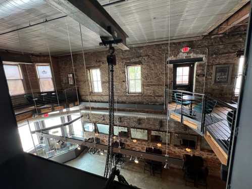 Interior view of a rustic, multi-level space with exposed brick walls, large windows, and industrial-style decor.