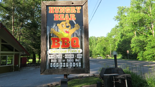 Sign for Hungry Bear BBQ featuring a bear mascot, offering dine-in or carry-out options for various meats.