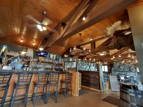 Cozy restaurant interior featuring a wooden bar, high stools, and rustic decor, including a mounted moose head.