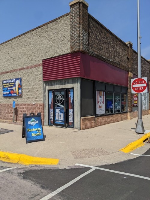 Exterior of a building with a sign for "The Den" and a promotional sign for Business Month. Clear blue sky above.