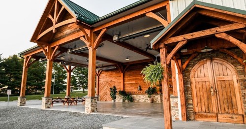 A rustic building with wooden beams, a stone entrance, and a spacious outdoor area surrounded by greenery.